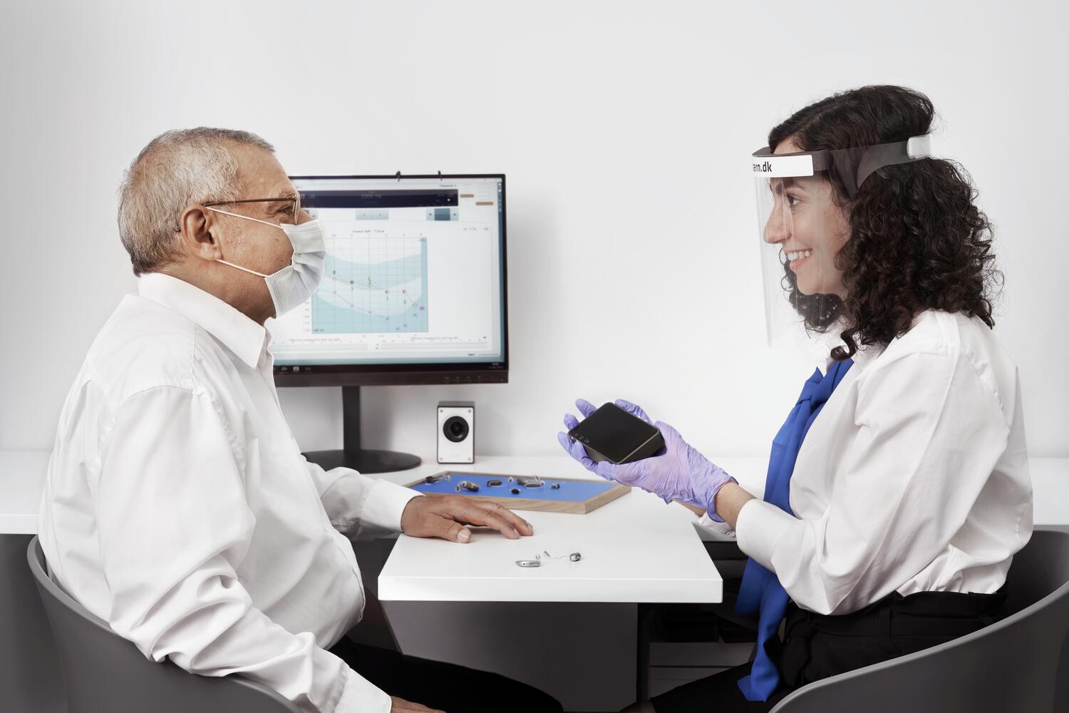 client sitting across from hearing professional showing hearing aids in a hearing clinic