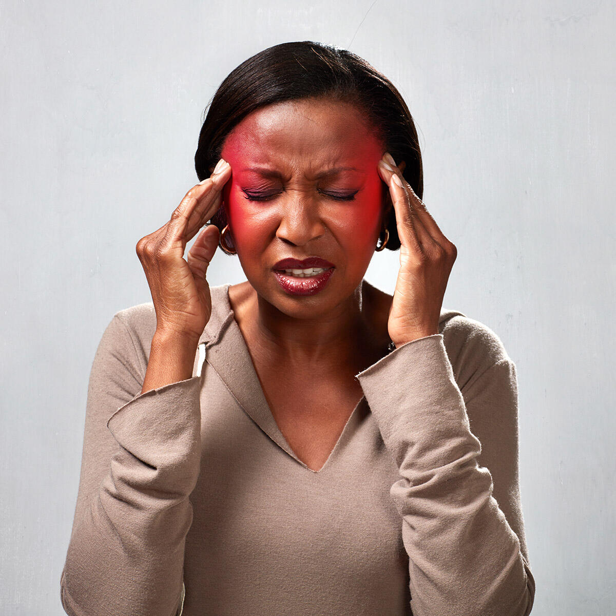 woman with hands to her temples. Red radiates from under her finger tips and she wears a painful expression.