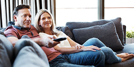 man turning up the volume while watching tv with his wife