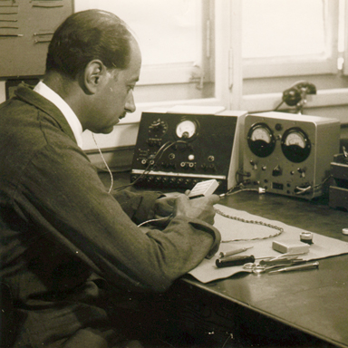 Old black and white photo of man sitting by desk testing Bernafon hearing aids, around 1950