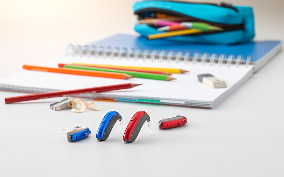 The Bernafon Leox Super Power | Ultra Power behind-the-ear hearing aids in front of colored crayons and other school materials.