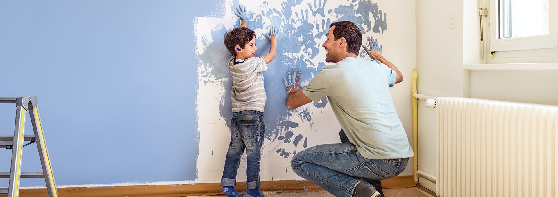 Father and son with Bernafon Leox Super Power|Ultra Power hearing aids painting a wall and spontaneously adding hand prints.