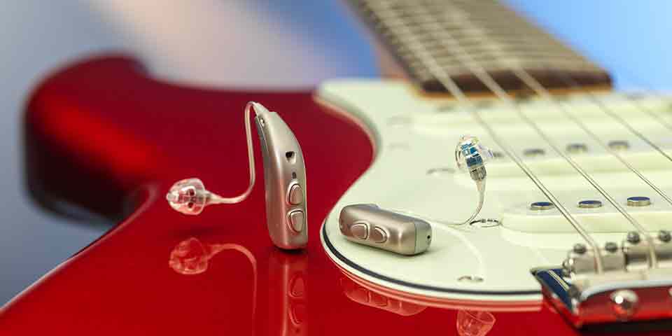 Les nouvelles aides auditives rechargeables au lithium-ion Viron miniRITE T R de Bernafon sur une guitare électrique rouge montrant les reflets de l'appareil.