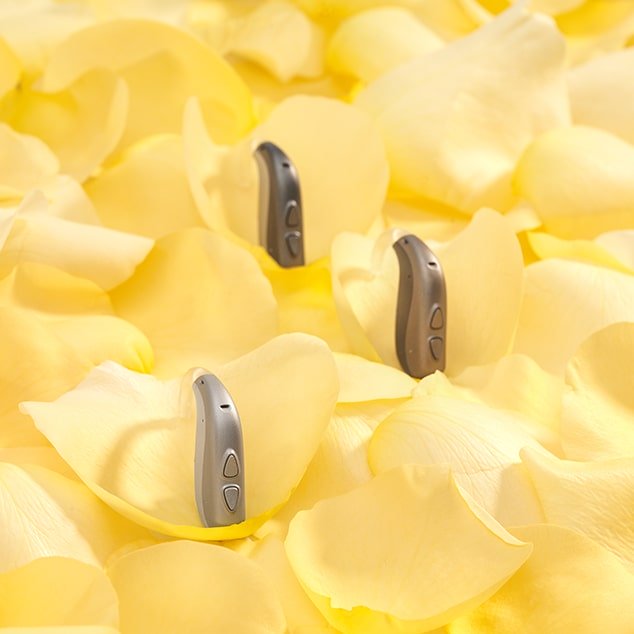 Three Bernafon behind-the-ear Nevara hearing aids on yellow flower petals