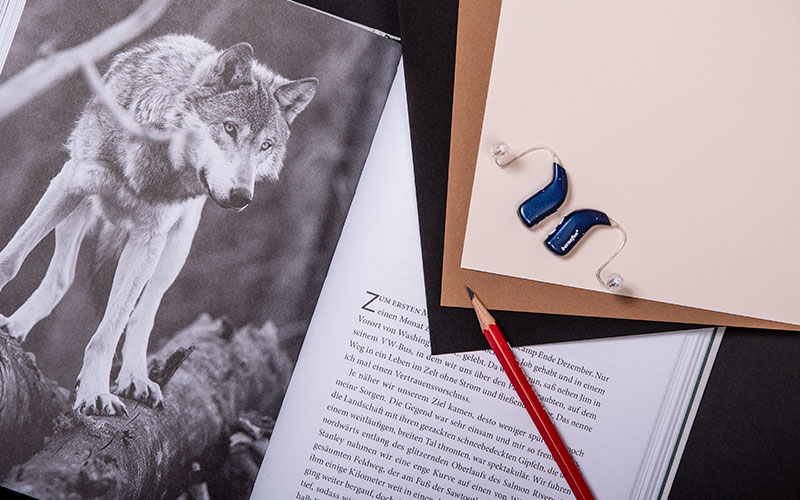 Appareils auditifs rechargeables Alpha bleu nuit placés sur un livre avec une image de loup à côté d'un crayon rouge