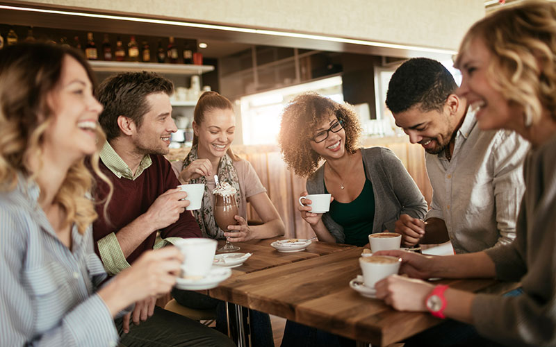 Happy people sitting around a table drinking coffee to show listening situation of Bernafon Alpha rechargeable hearing aids 