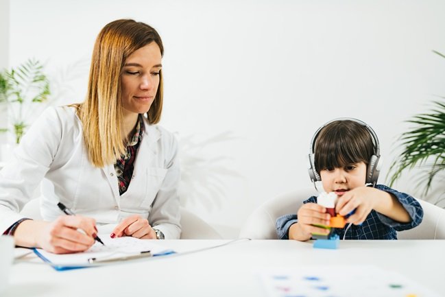 physician testing hearing while child plays with blocks