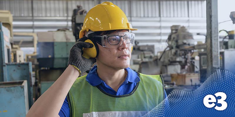 An asian man in industrial building with hard hat and earmuffs