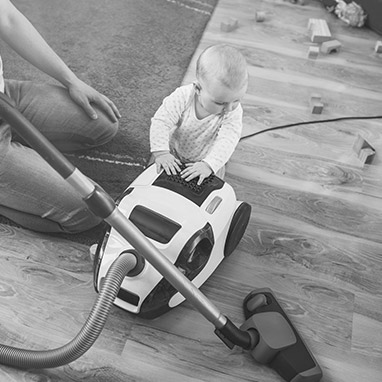 Infant standing against a vacuum cleaner